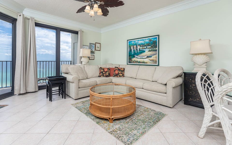 Cozy living area features a light-colored sectional sofa with floral accents, a glass-top coffee table, and gulf views