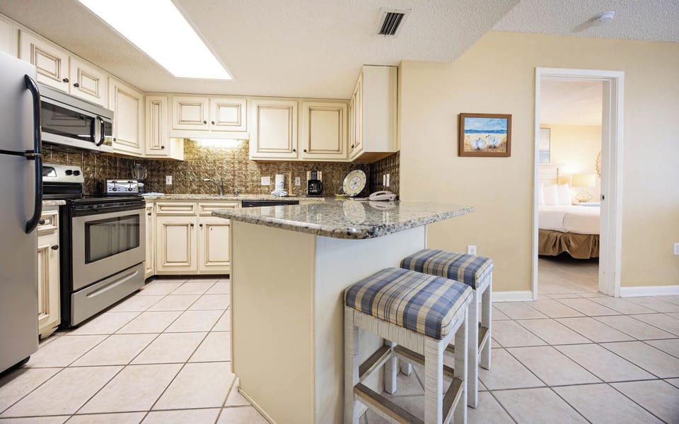 Kitchen features granite countertops, light cabinetry, and a breakfast bar with seating, leading to the master suite