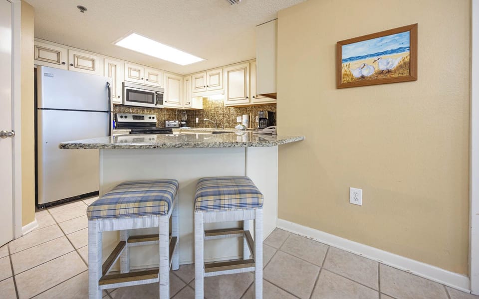 Bright kitchen area features granite countertops, white cabinetry, and a breakfast bar with seating for casual dining