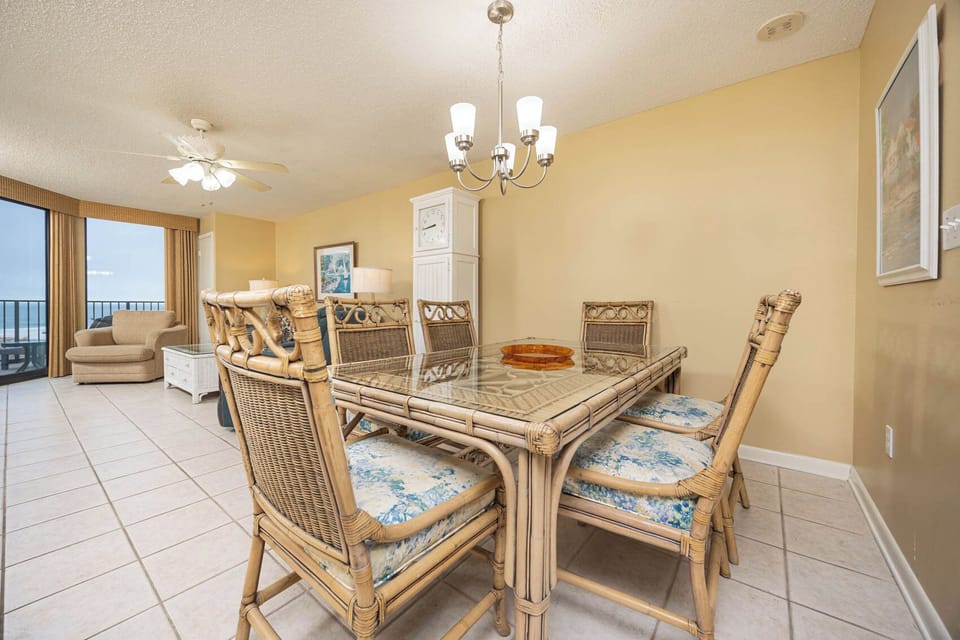 Dining area features a glass-top table with rattan chairs, complemented by a cozy seating nook and views of the gulf