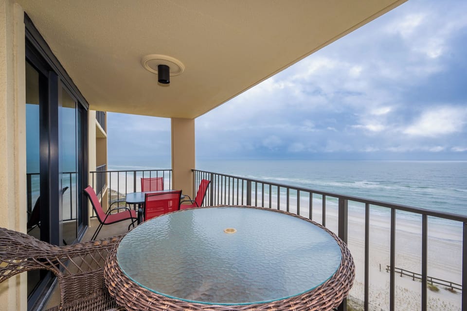 Enjoy breathtaking views from this balcony featuring a glass-top table and vibrant red chairs, perfect for relaxation