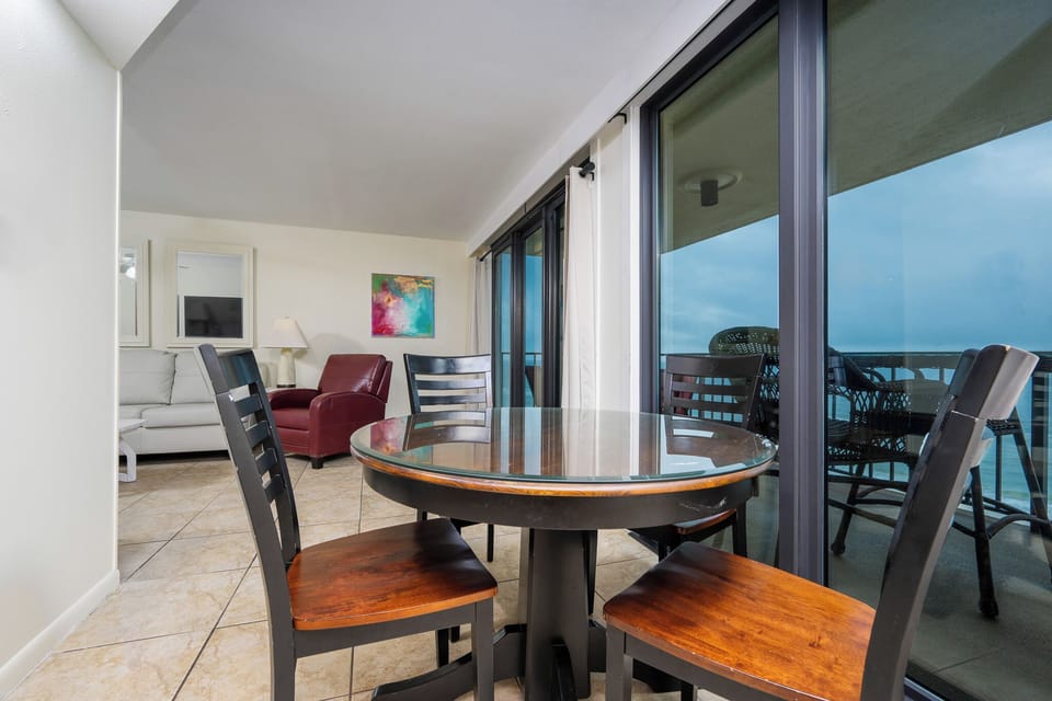 This inviting living area features a round dining table, a cozy red chair, and stunning views from the large glass doors
