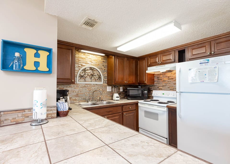 This kitchen features rich wooden cabinetry, a stylish backsplash, and essential appliances, perfect for meal preparation