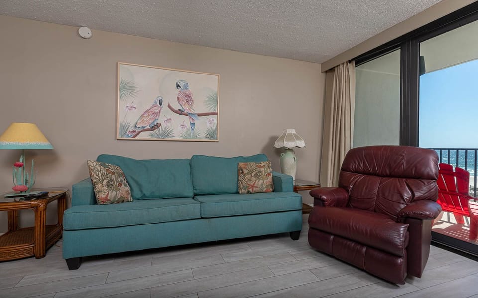 This cozy living area features a teal sofa, a recliner, and a stunning beachfront view through large windows
