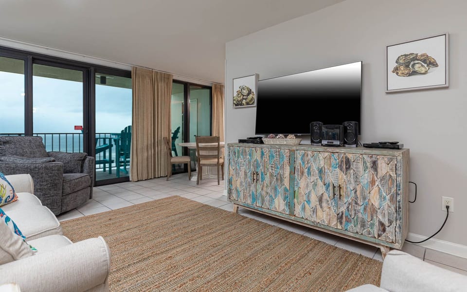 This inviting living area features a large TV, queen sofa-sleeper, colorful decor, and a view of the beachfront balcony