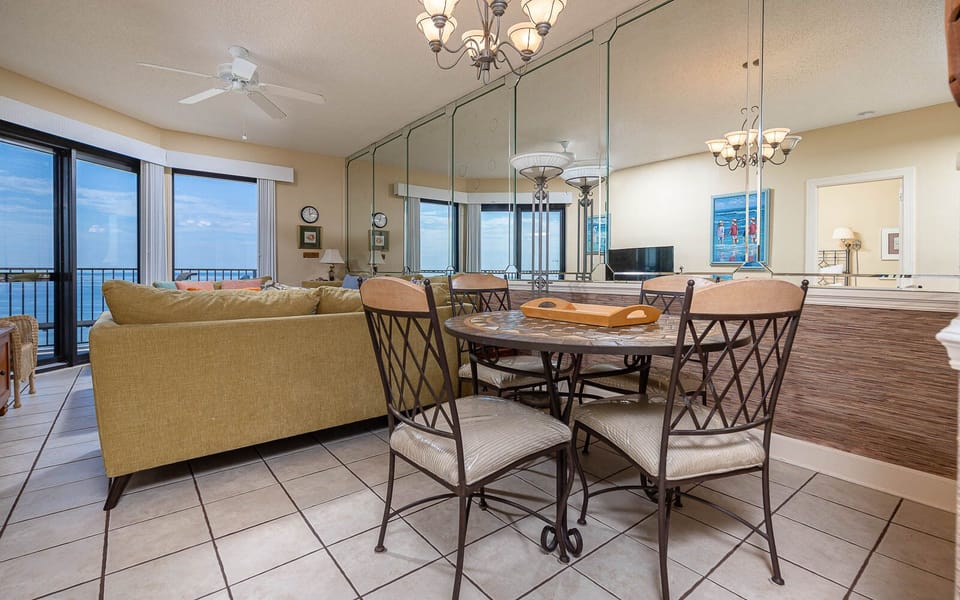 Cozy seating area features a plush sofa and a round dining table, with expansive windows offering a view of the gulf