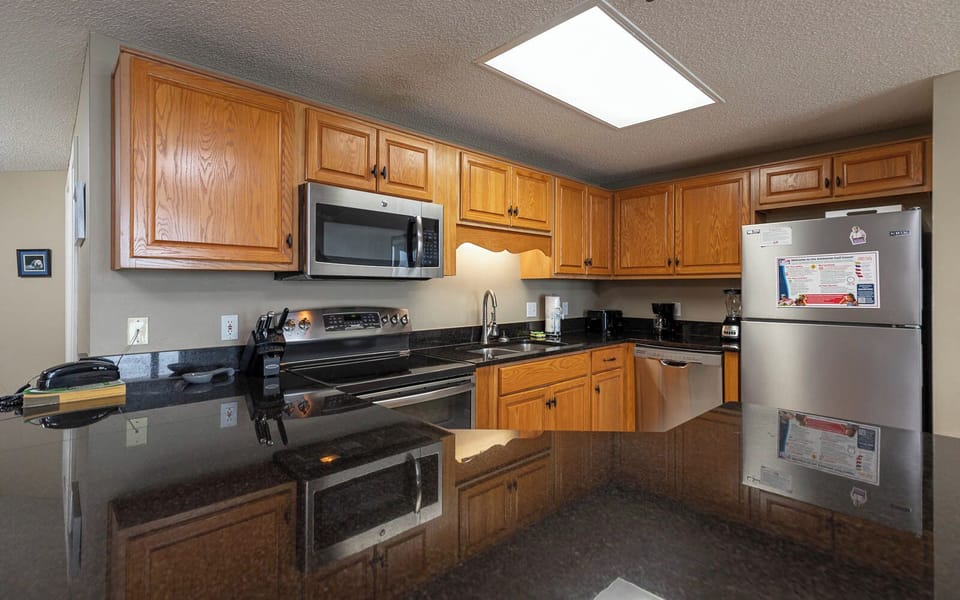 Sleek black countertops, stainless appliances, and rich wooden cabinetry in this inviting kitchen