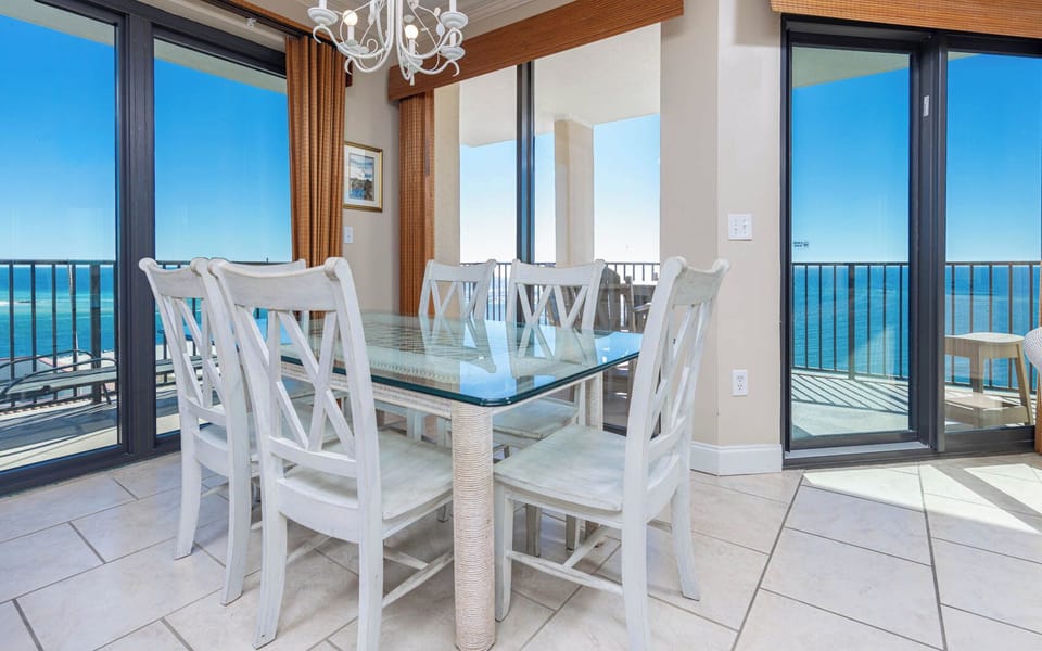 Gather around the glass-top dining table with views of the beach and natural light streaming through the large windows