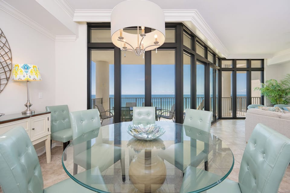 Bright dining area with mint green chairs and a stunning coastal view through floor-to-ceiling windows