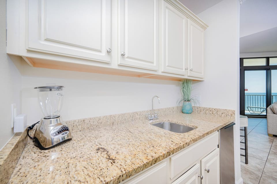 Wet bar with granite countertops, a modern sink, and a glimpse of the stunning coastal view beyond