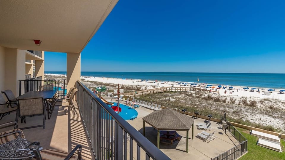 The balcony features a dining table with chairs, offering a second floor view of the beach, pool area, and pirate splash park