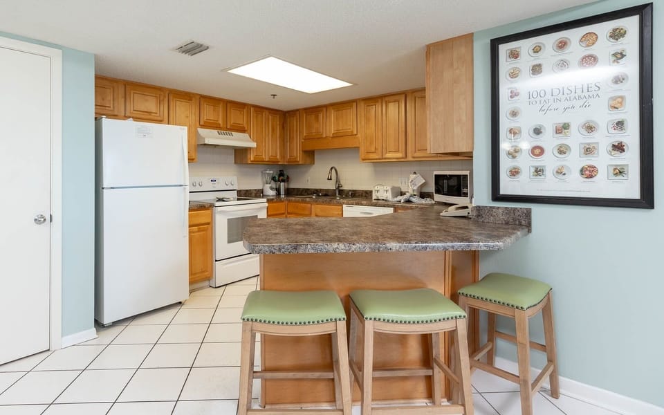 The fully-equipped kitchen features warm wood cabinetry, a stylish countertop, and a breakfast bar with green-topped stools