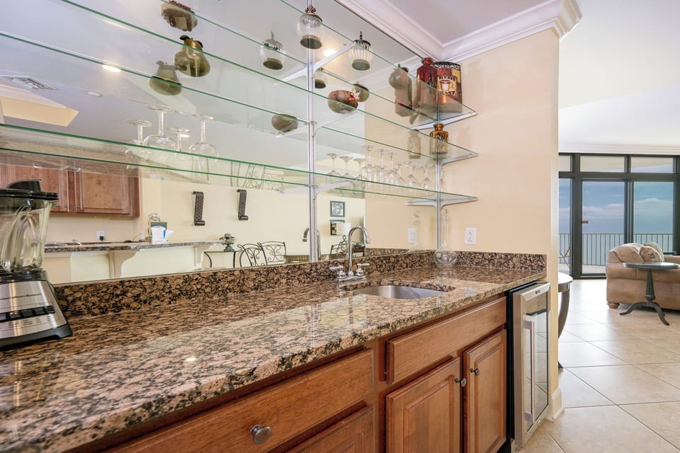 Elegant granite countertops, glass shelves, and wine cooler enhance this inviting wet bar with a glimpse of the beach beyond