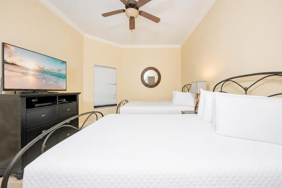 Bright guest bedroom featuring two comfortable queen beds and a large TV for entertainment