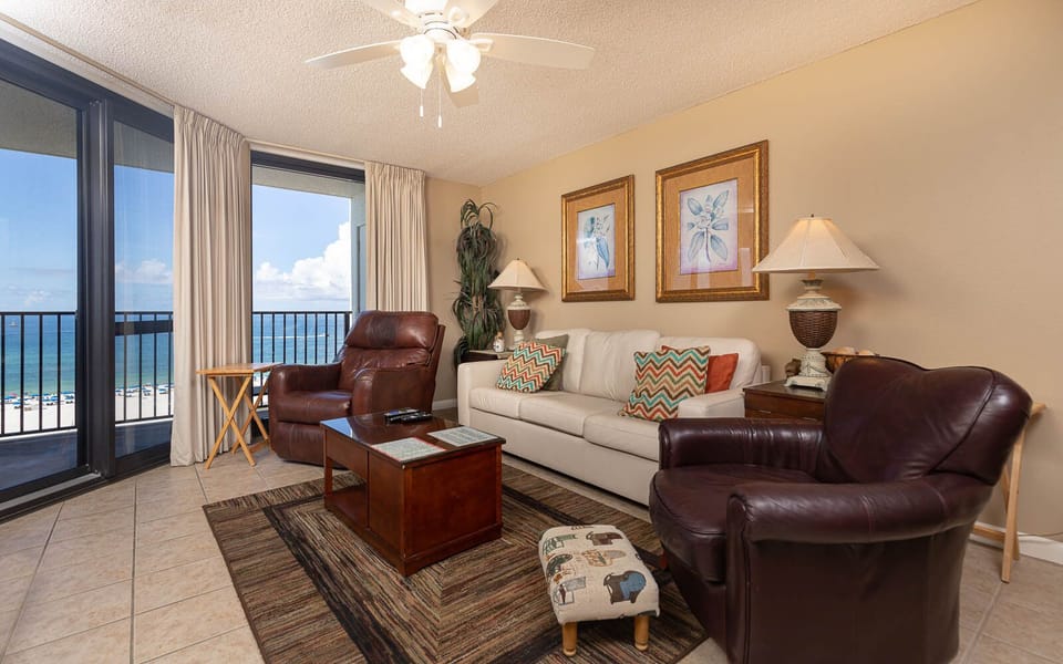 The living area features a light sofa with queen sleeper, leather chairs, and expansive views of the beach