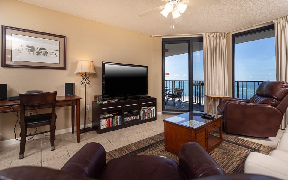 Cozy living area features a large TV, a comfortable brown recliner, and access to a balcony with a view of the gulf