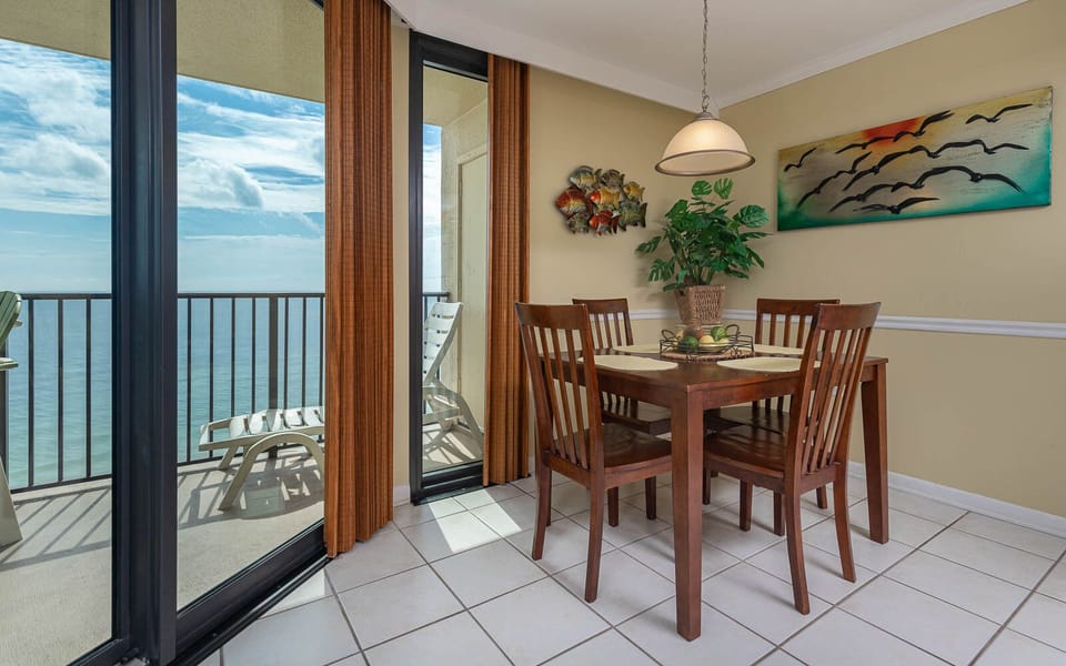 The dining area features a wooden table with four chairs, vibrant artwork, and sliding glass doors leading to the balcony