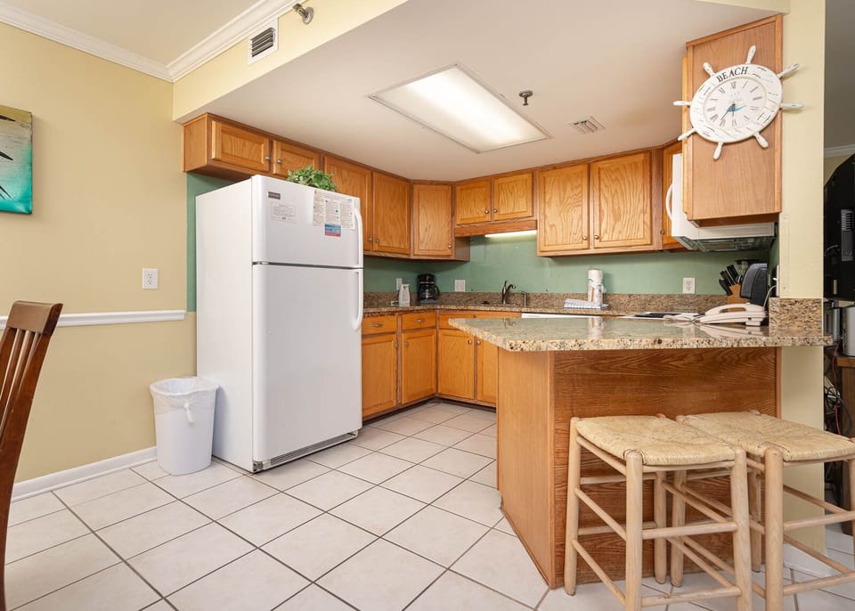 The kitchen features wooden cabinetry, white appliances, and a granite-topped island with two woven stools