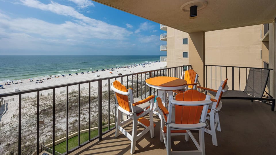 Relax on the balcony with vibrant orange chairs, enjoying a beautiful view of the beach and gentle waves