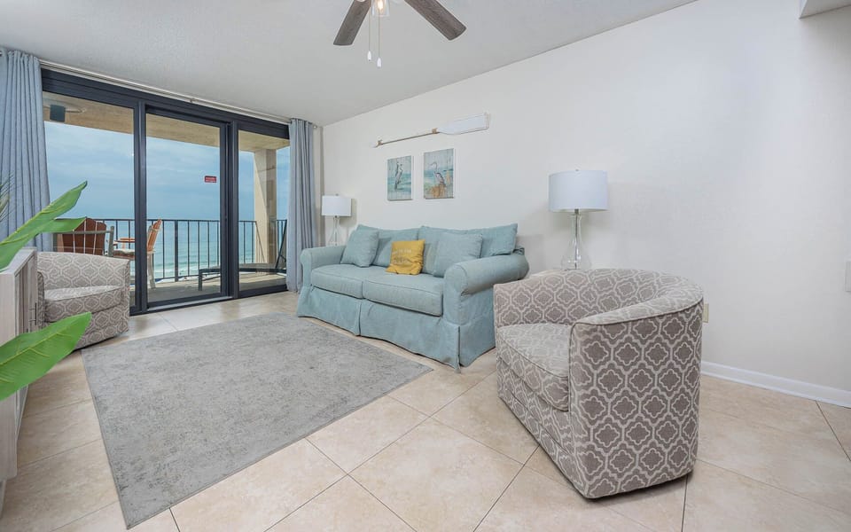This living area features a cozy sofa with queen sleeper, stylish chairs, and a breathtaking beach view from the balcony