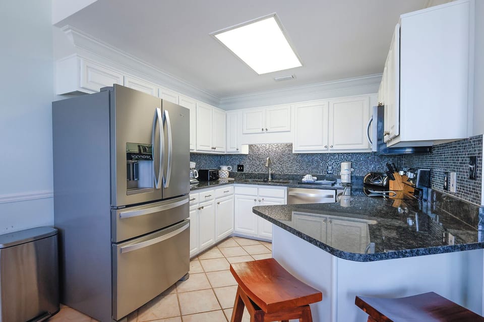 Bright kitchen features sleek cabinetry, a granite countertop, and a breakfast bar with seating, perfect for casual dining