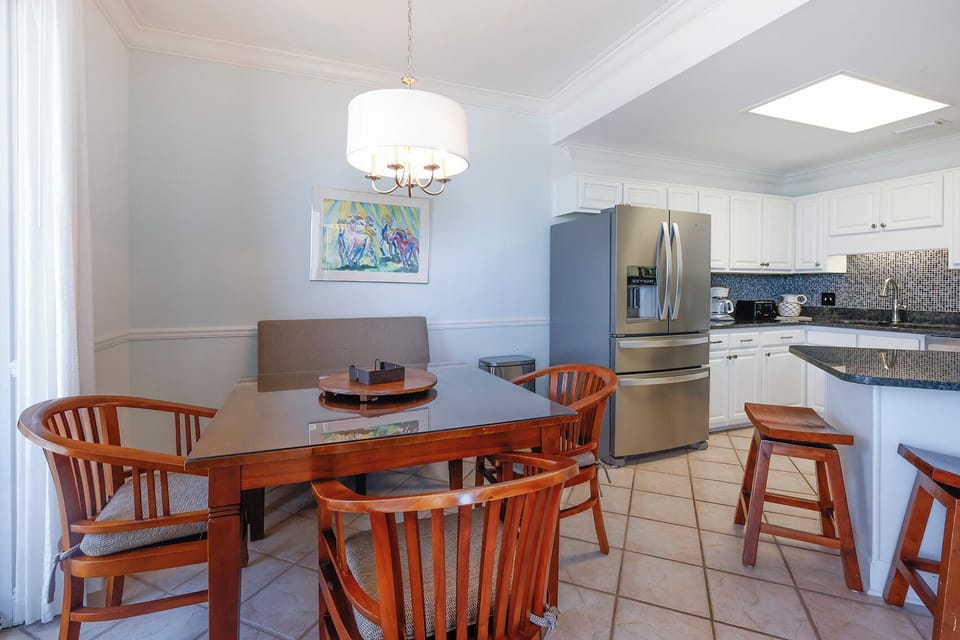 Kitchen and dining area features a wooden table surrounded by chairs, with a breakfast bar and stylish art on the wall