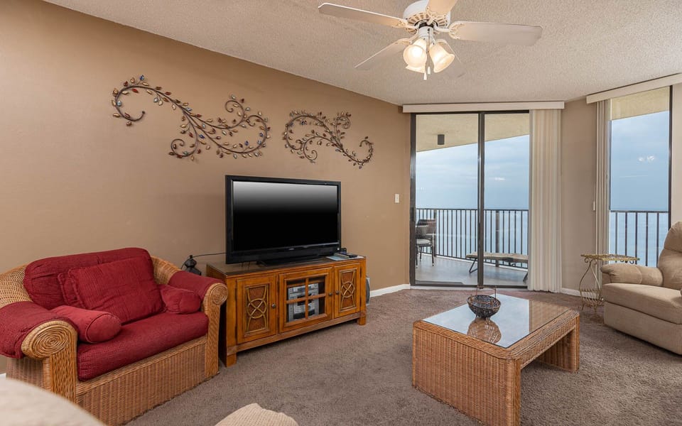 Living area features a red sofa with queen sleeper, wooden entertainment unit, and a balcony with beach front views