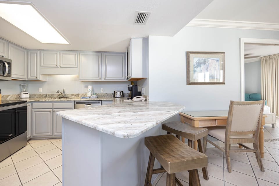 The kitchen area features light gray cabinetry, a marbled countertop, Keurig coffee maker, and a breakfast bar with stools