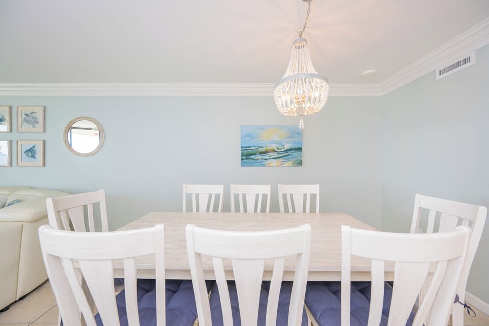Soft cushions support you at the dining table where coastal art and a beaded chandelier brighten the space