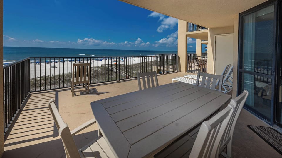 The spacious extended balcony features a dining table with chairs, offering a direct view of the beach and inviting waves