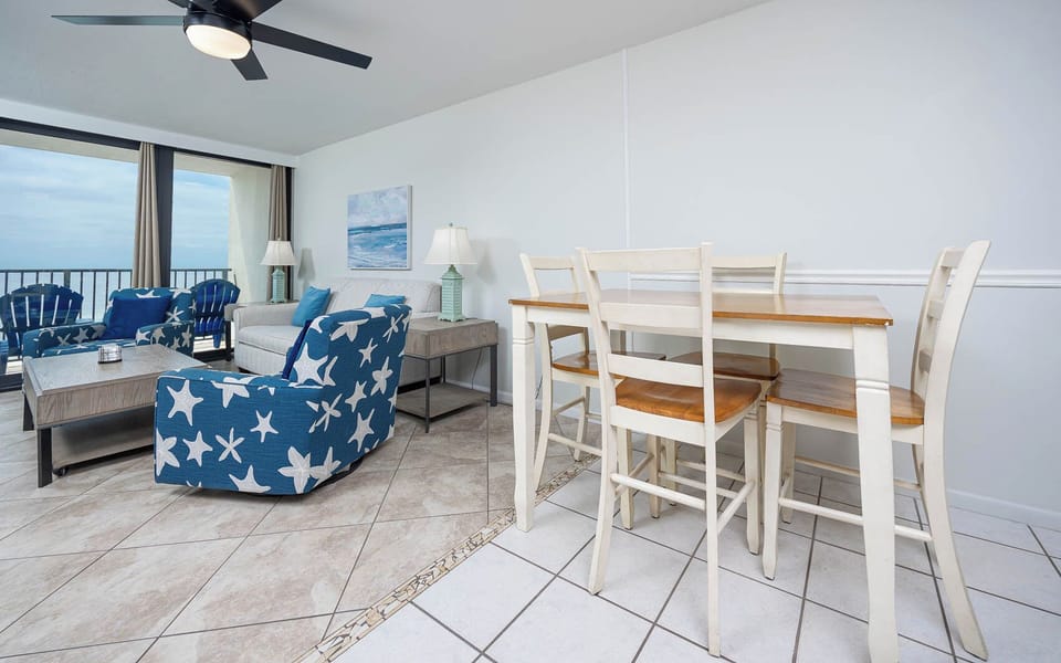 The living area features blue starfish-patterned chairs, a cozy sofa, and a stunning beachfront view through large windows