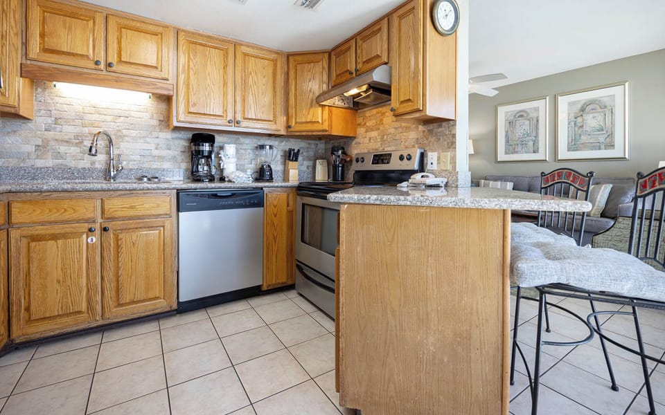Kitchen featuring wooden cabinetry, granite countertops, and stainless appliances, with a view of the beachfront balcony