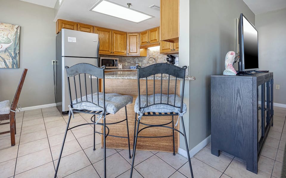 The kitchen area features wooden cabinets, a granite countertop, and two high-top chairs, creating a welcoming space