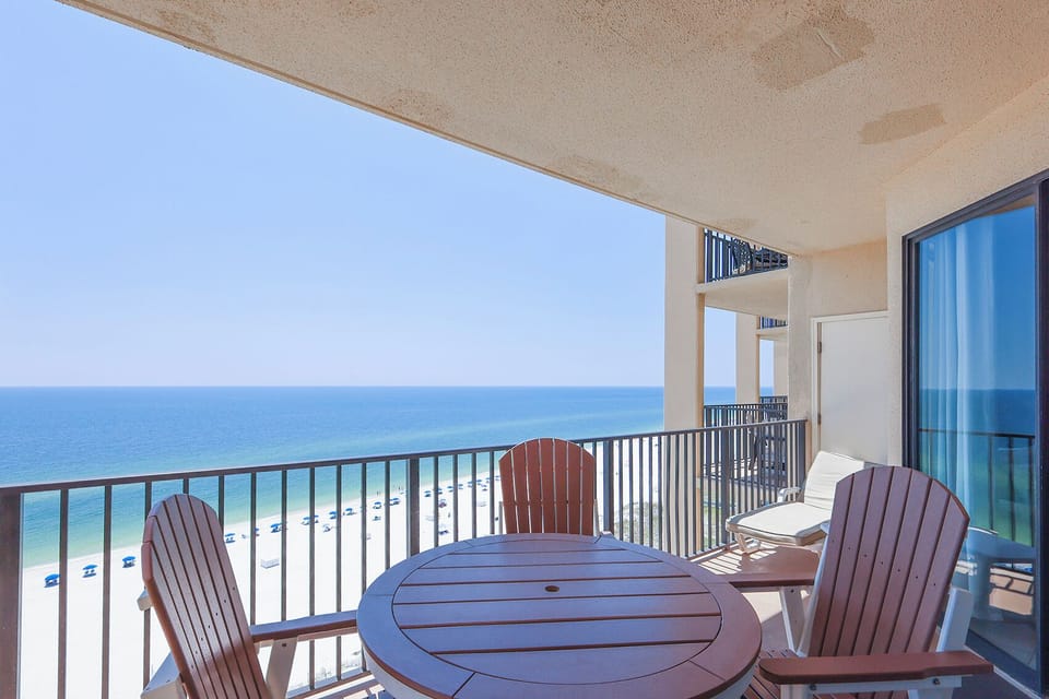 Relax on the balcony, featuring a round table and Adirondack chairs, with a view of the beach and turquoise waters
