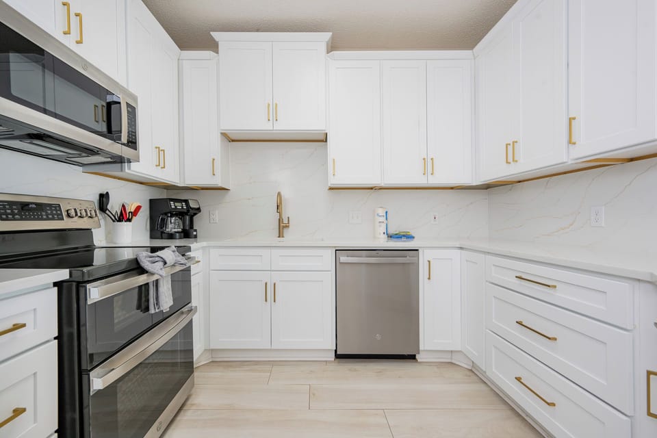 You find ease in preparing meals surrounded by gleaming white cabinets and gold-tone fixtures in the kitchen