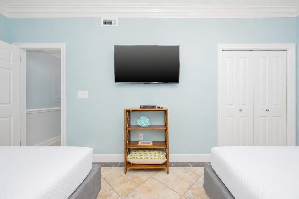 Light blue walls complement two queen beds, with a mounted TV and stylish shelving adding comfort to the guest room