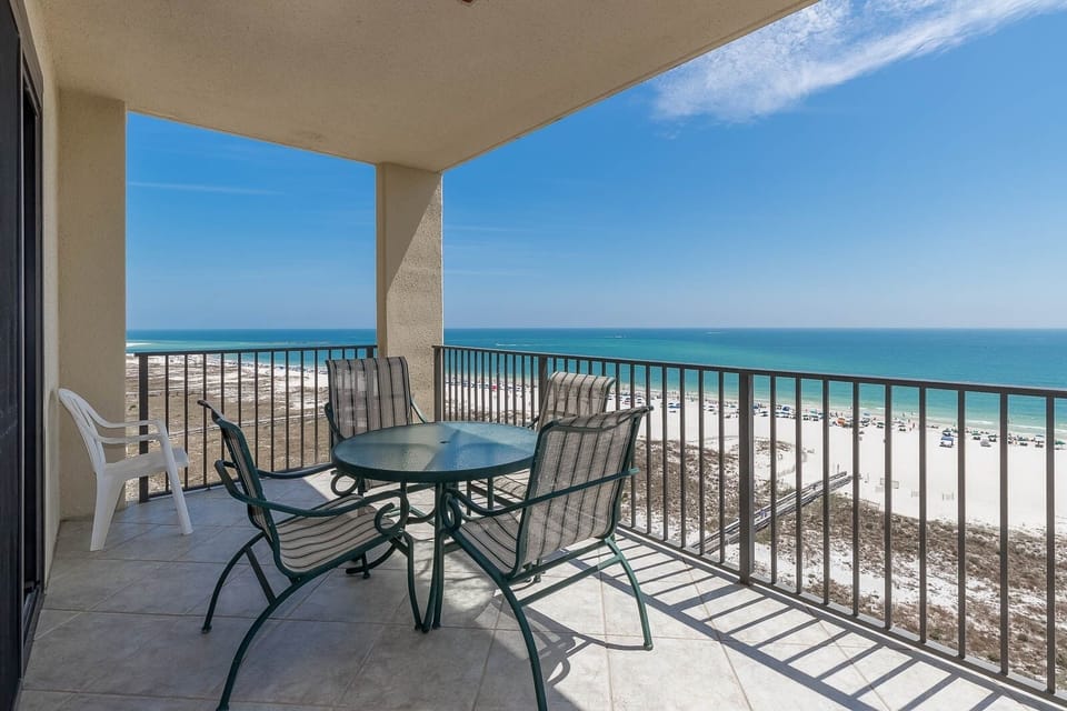 Balcony with a round table and chairs offers a panoramic view of the beach and turquoise gulf waters below
