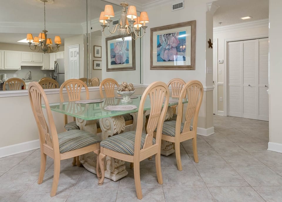 Elegant dining area features a glass-top table with six wooden chairs, complemented by warm lighting and decorative artwork