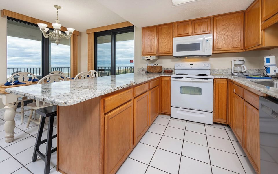 Kitchen area features wooden cabinetry, granite countertops, and a breakfast bar with seating, offering views of the beach