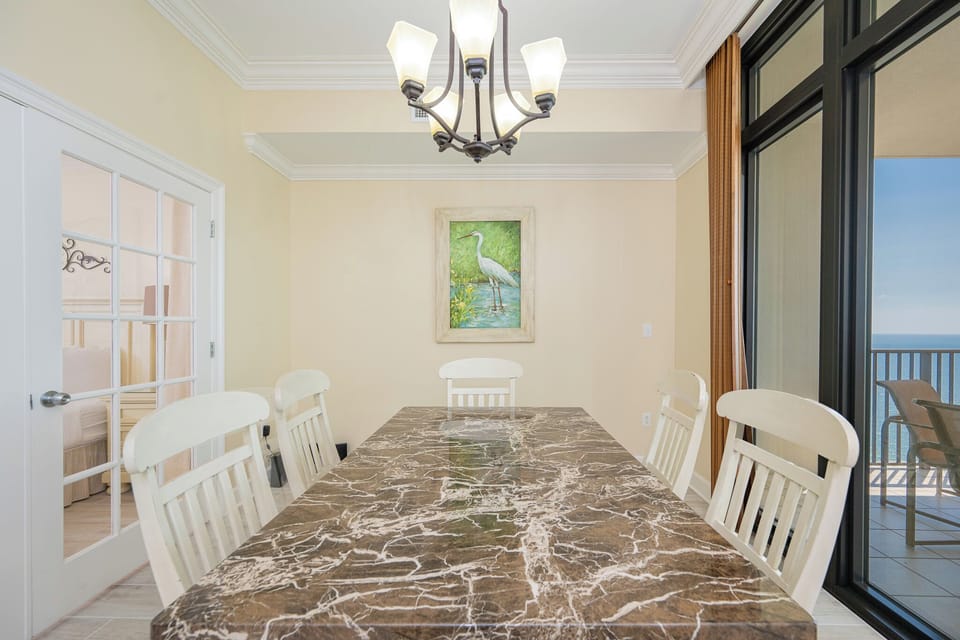 Bright dining area featuring a marble table, white chairs, and a beautiful view through large windows