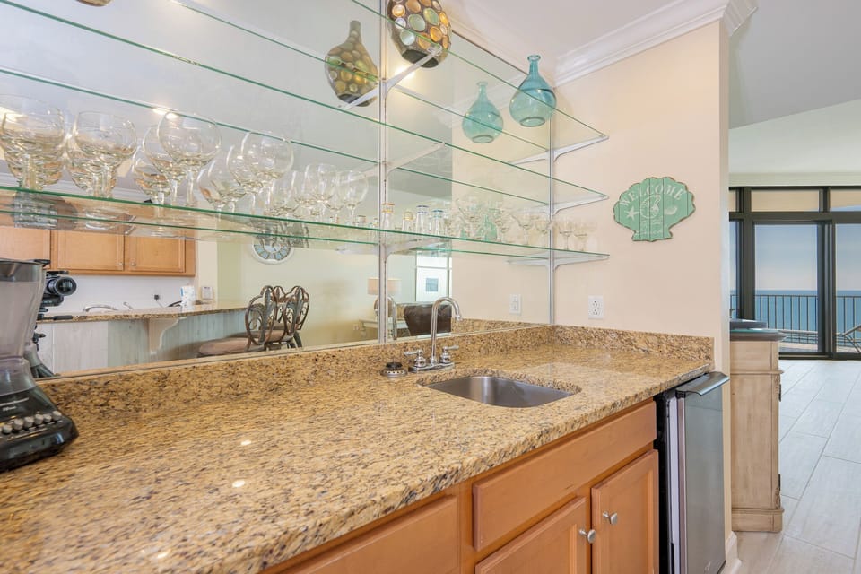 Wet bar area with granite countertops and glassware create an inviting atmosphere in this modern kitchen with a scenic view