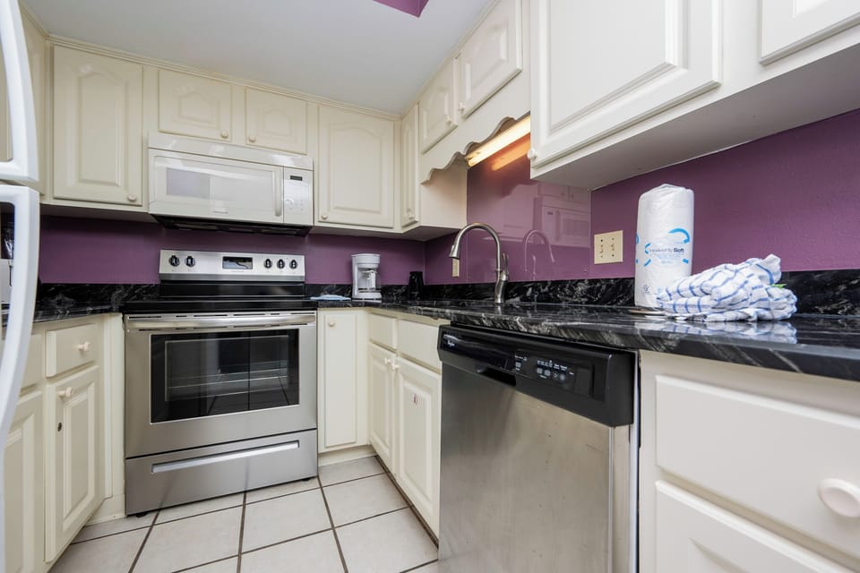 The kitchen features sleek stainless appliances, granite countertops, and a vibrant purple wall for a cheerful cooking space