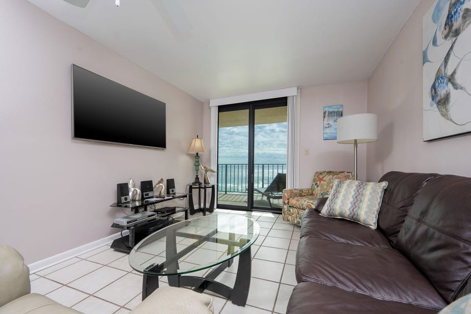 This living area features a large TV, a cozy seating arrangement with queen sofa-sleeper, and a beautiful balcony view