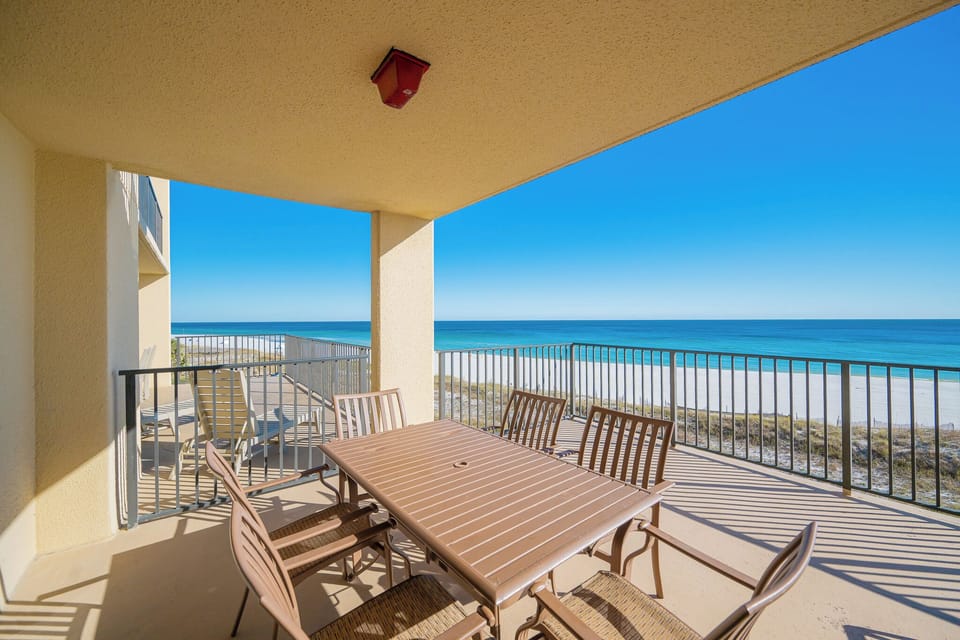 The spacious extended balcony features a dining table with seating, offering direct views of the tranquil beach