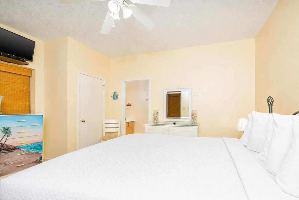 This bright guest bedroom features a king bed with crisp white linens, a colorful dresser, and a cozy chair for relaxation