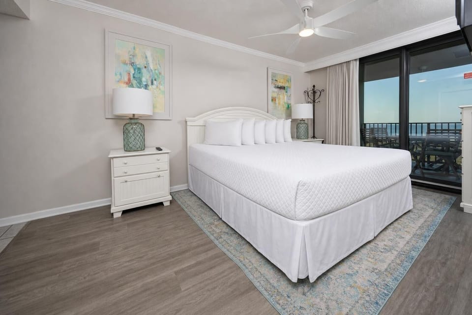 Soothing master bedroom features a plush king bed, coastal artwork, and access to the balcony with a view of the beach