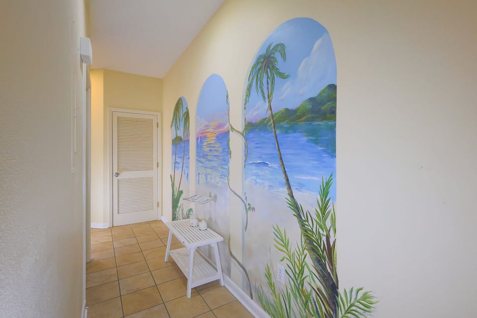 A vibrant mural of palm trees and a serene beach scene enhances the welcoming hallway, complemented by a white side table