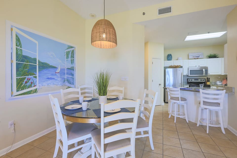 Dining area featuring a round table with white chairs, complemented by a vibrant mural and a modern breakfast bar