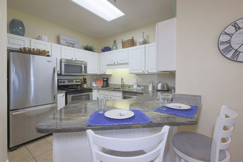 Bright kitchen featuring white cabinetry, granite countertops, and a breakfast bar with nautical-themed decor
