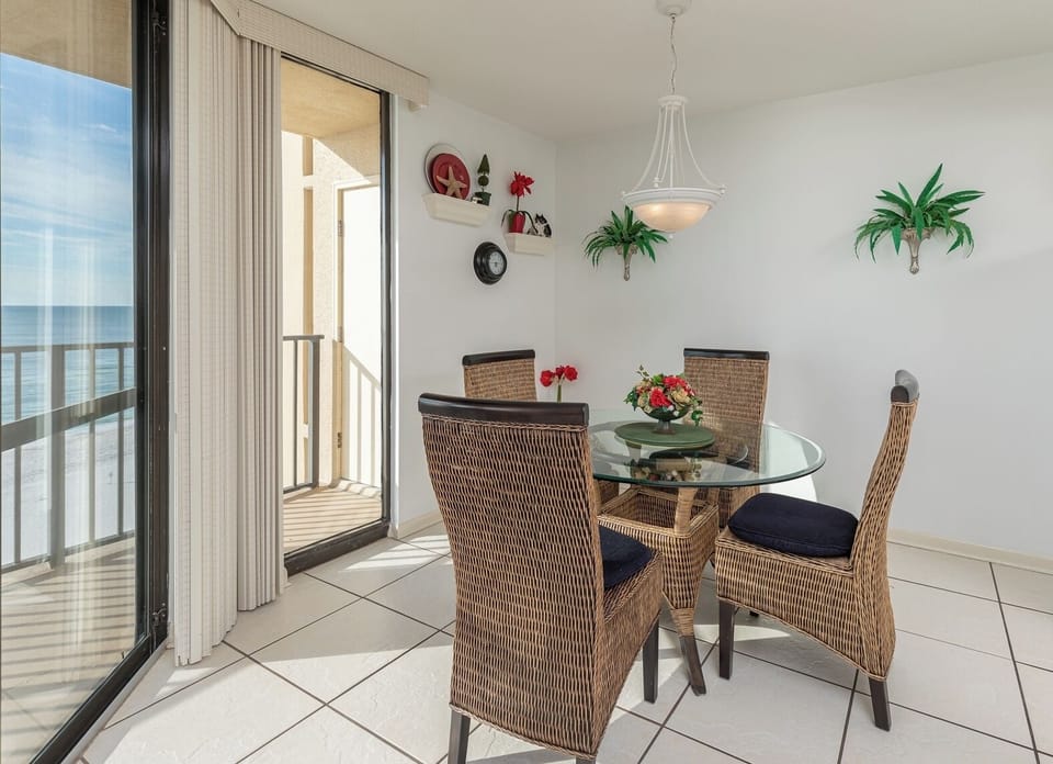A dining area features a glass table surrounded by stylish chairs, with a view of the beach